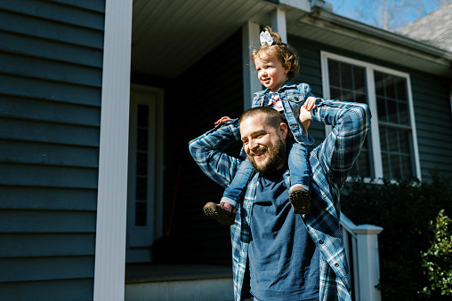 Young father carrying his toddler daughter on shoulder around house